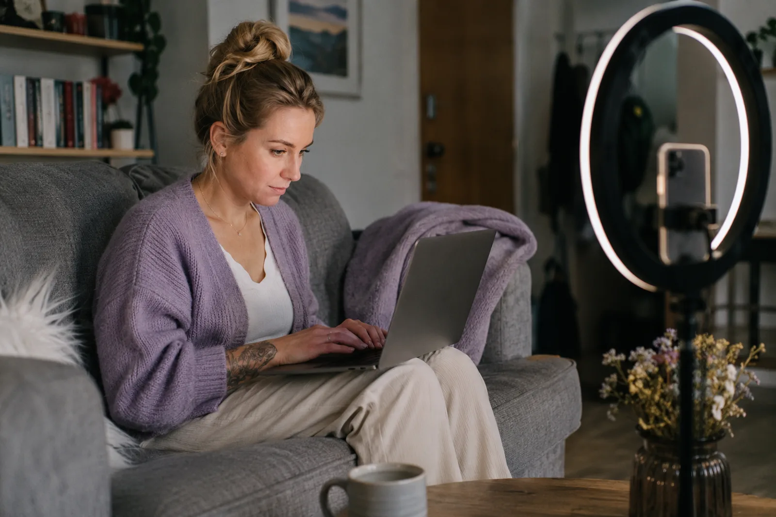 A creator on her couch with a laptop on her knees, a phone on a ring light beside her, reading over a pitch before she sends it.