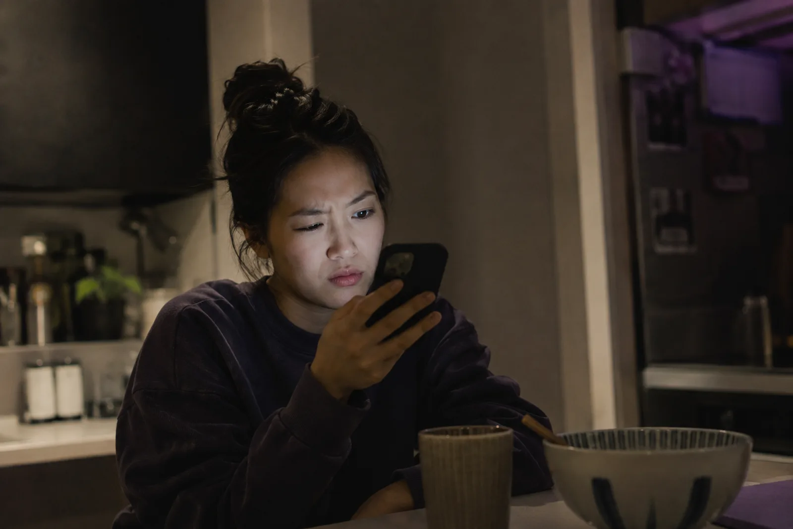 A creator in a dim kitchen at night, face lit by her phone, reading an offer that doesn't add up.